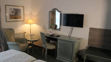 Habitación de hotel con cama, escritorio, silla, lámpara, televisor y un cuadro en la pared.
