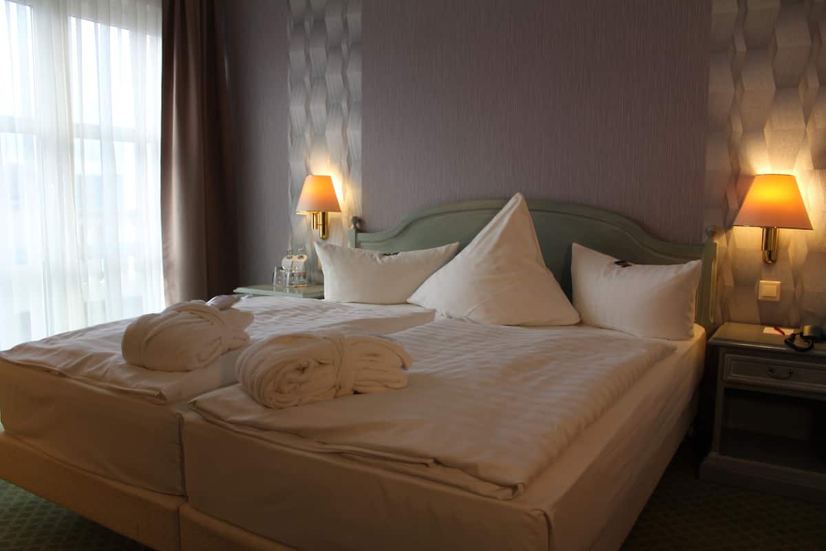 Een hotelkamer met een groot bed, twee bedlampjes en een raam met gordijnen.