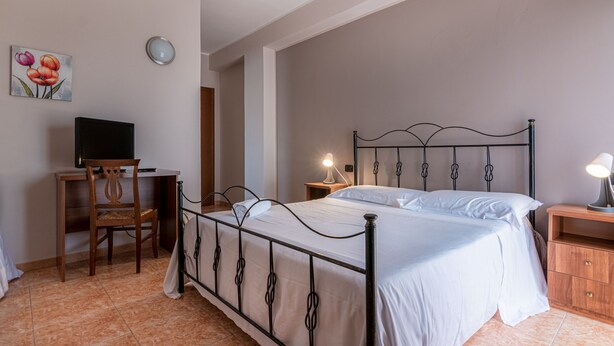 A bedroom with a bed, a desk, a chair, a nightstand, and a wall clock.