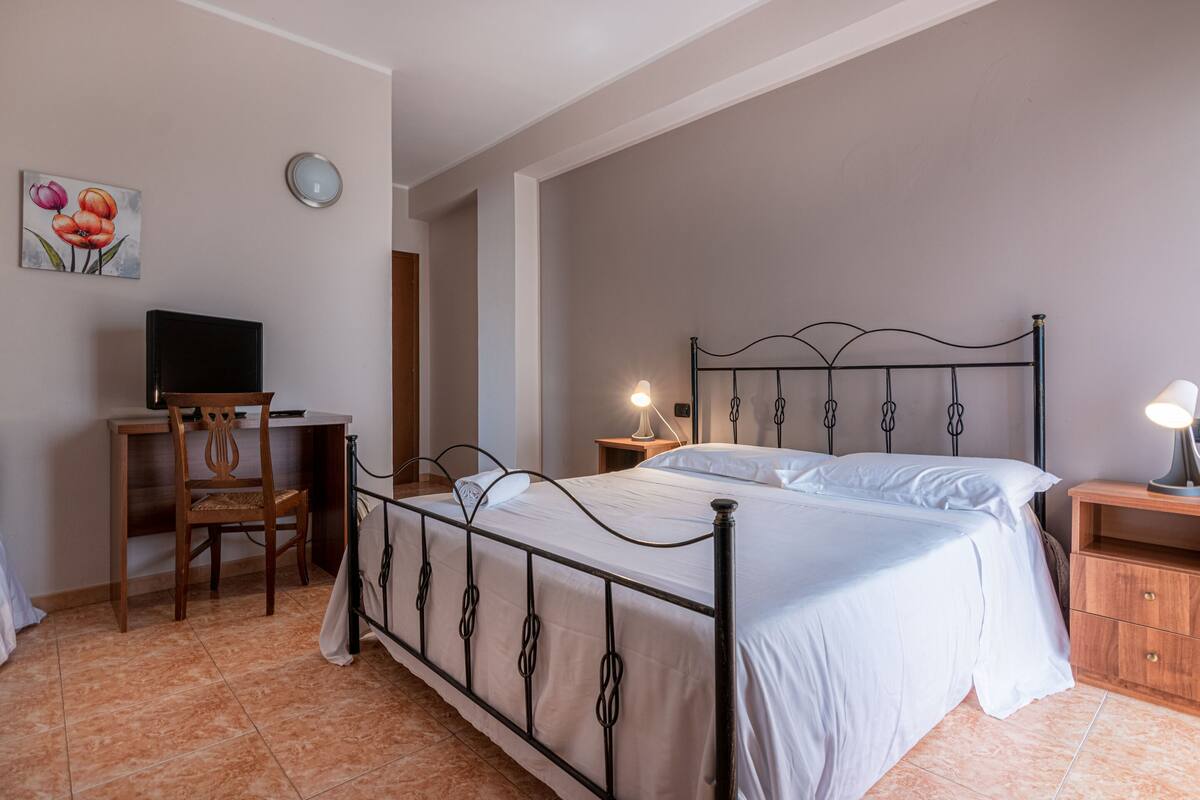 Ein Schlafzimmer mit Bett, Schreibtisch, Stuhl, Nachttisch und Wanduhr.