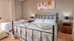A bedroom with a metal bed frame, two bedside tables, a nightstand, a wall-mounted air conditioner, and a floral painting.