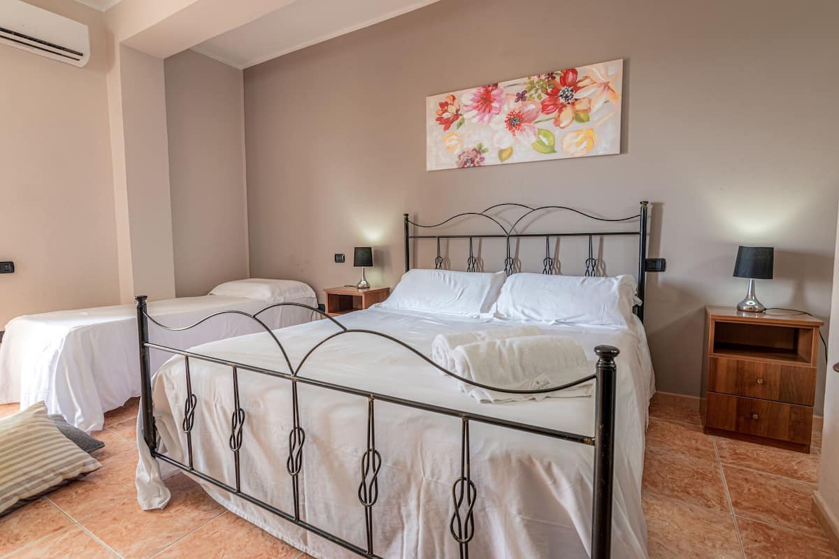 Ein Schlafzimmer mit einem Metallbettgestell, zwei Nachttischen, einem Wandklimagerät und einem floralen Gemälde.