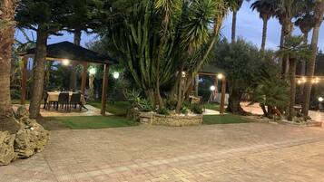 A paved outdoor area with a covered seating area, surrounded by palm trees and a statue.