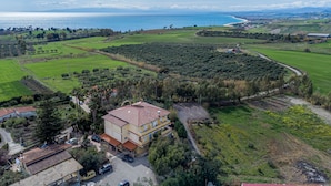 A coastal property with a large house, a driveway, parked cars, and surrounding green fields.