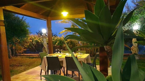 An outdoor dining area with a covered pergola, a table set for two, and a statue in the background.