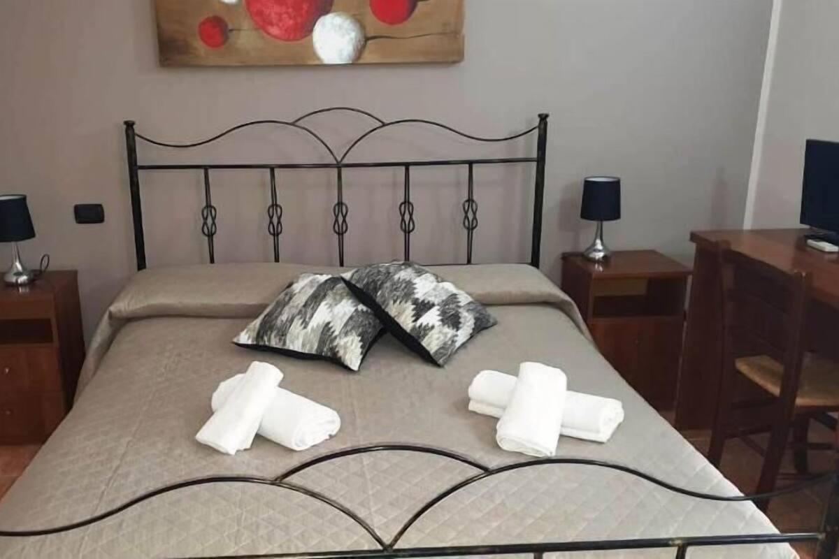 Ein Bett mit Metallgestell, zwei Kissen, eine Decke und zwei Nachttische mit Lampen.