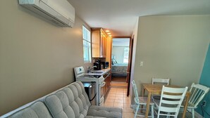 A compact living space with a sofa, dining table, chairs, kitchenette, and a small bedroom. - Pine View Lodge (Old Orchard Beach)