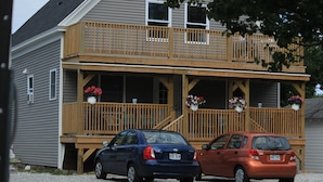A two-story house with a wooden deck and a car parked in front. - Pine View Lodge (Old Orchard Beach)