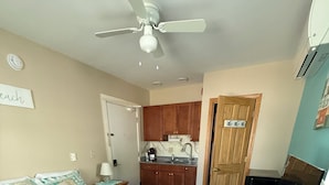 A bedroom with a bed, a desk with a computer, a ceiling fan, and a kitchenette. - Pine View Lodge (Old Orchard Beach)