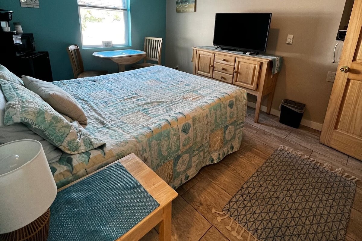 A bedroom with a bed, a desk, a television, and a window.