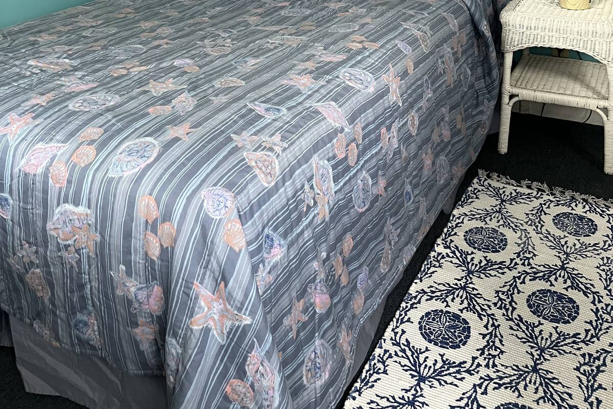 A bedroom with a bed, a nightstand, a lamp, a framed picture, and a rug.