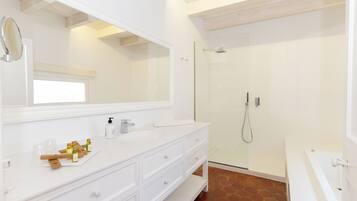 Un baño moderno con un tocador blanco, un espejo grande, cabina de ducha con mampara de vidrio y una bañera blanca.