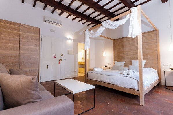 Un dormitorio con cama con dosel, un sofá, una mesita y un armario de madera.
