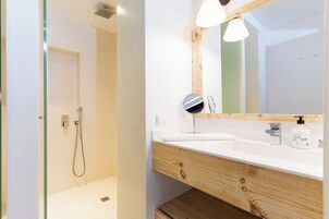 Un baño moderno con cabina de ducha de vidrio, tocador de madera con espejo y lavamanos blanco.