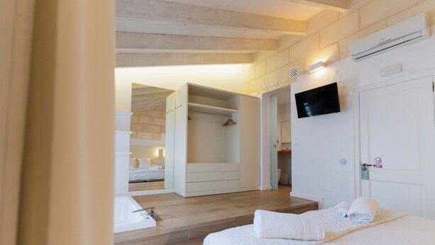 A hotel room with a wooden floor, a bed with white linens, a TV mounted on the wall, and a closet with a mirror.