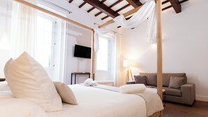 A hotel room with a large bed, a sofa, a television, and a window with curtains.