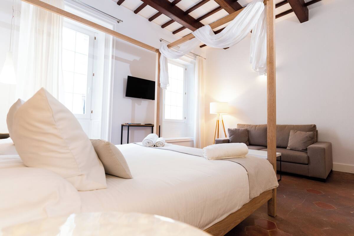 A hotel room with a large bed, a sofa, a television, and a window with curtains.