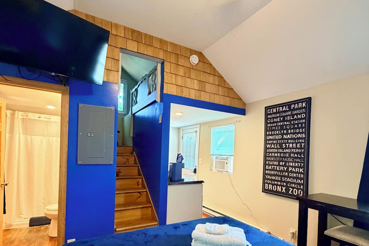 A bedroom with a bed, a staircase, a bathroom, and a wall sign listing NYC landmarks.