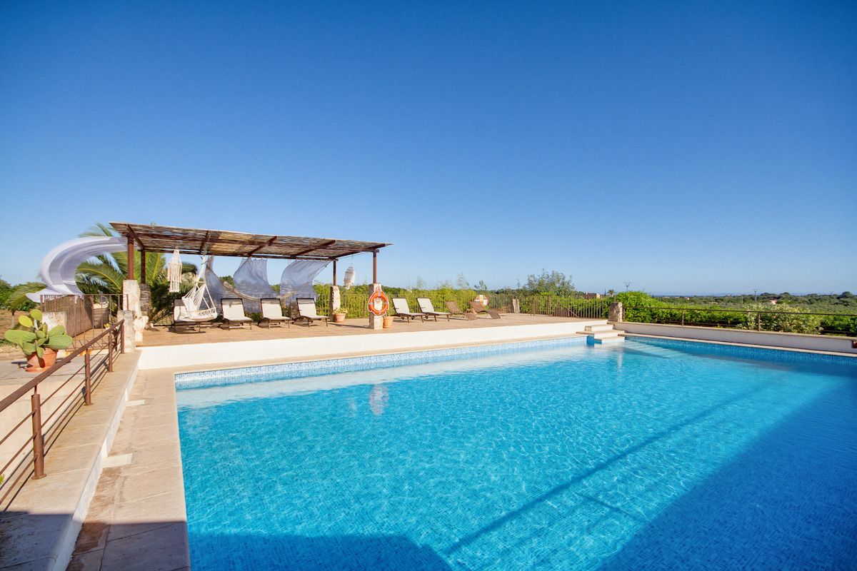 A clear blue pool with lounge chairs and a covered seating area.