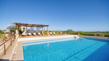 Una piscina azul cristalina con sillas de descanso y una zona de estar cubierta.