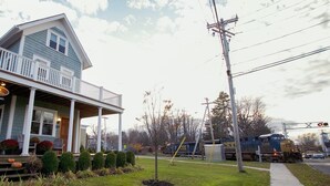 A two-story house with a porch, a small garden with pumpkins and flowers, and a train passing by on the tracks. - 24 East Main Street B&B (Canton)