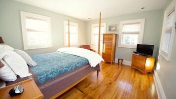 Un dormitorio con cama, cómoda, televisor y ventanas.