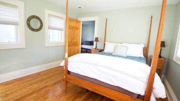Una cama con dosel en un dormitorio con piso de madera, dos mesitas de noche y una puerta que da a otra habitación.