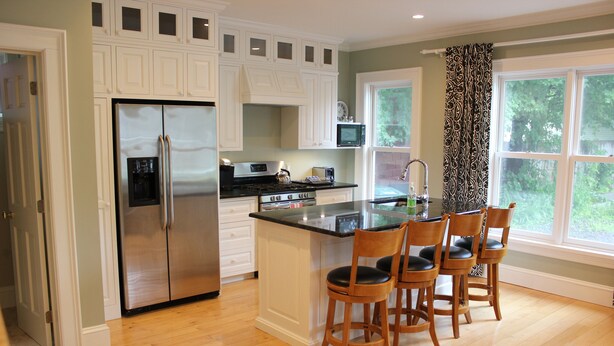 A kitchen with a stainless steel refrigerator, a microwave, and a coffee maker on the countertop. There are wooden chairs around a central island. - 24 East Main Street B&B (Canton)