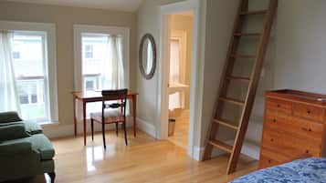 Ein Zimmer mit Holzboden, einem grünen Sofa, einem Holzschrank, einem Schreibtisch mit Stuhl und einer an der Wand angelehnten Leiter.