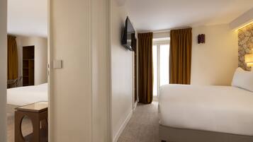 A hotel room with a bed, a TV mounted on the wall, a desk, and a window with curtains.