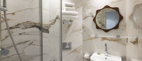 A bathroom with a glass-enclosed shower, a white sink, and marble walls.
