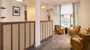 A hotel lobby with a reception desk, seating area, and a large window with curtains. - Hôtel Michelet Odeon (Paris)