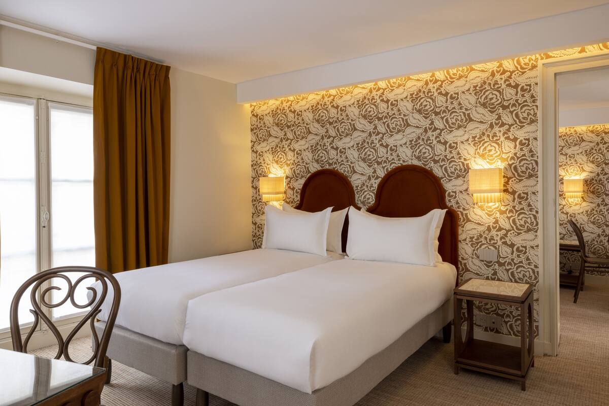 A hotel room with two beds, a small table, a chair, and a nightstand.