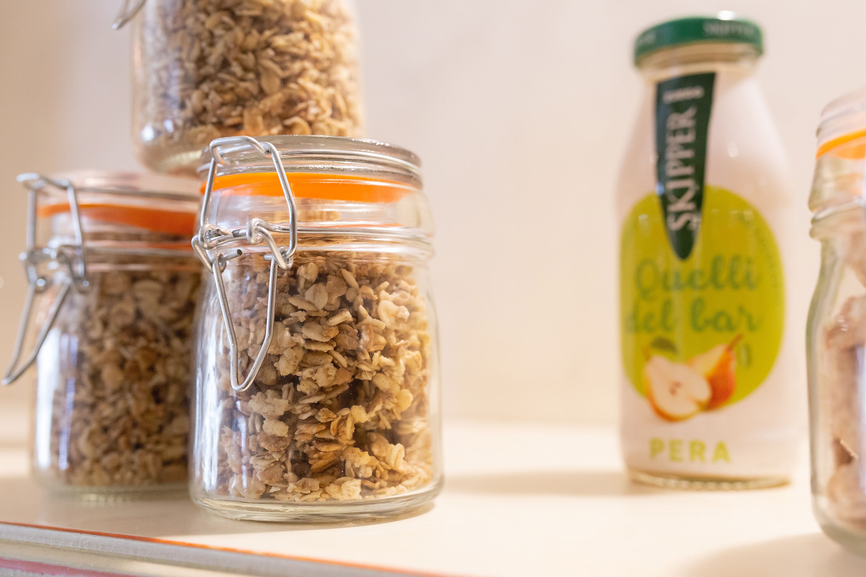 Tres frascos de vidrio con cierres metálicos que contienen granola, una botella de jugo de manzana Skipper's y un tarro de leche.