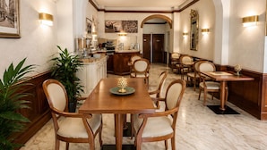 A spacious dining area with a marble floor, wooden furniture, and a central table with chairs. - Hotel Posta (Cecina)