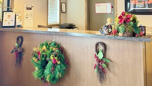 Zona de recepción de un hotel con mostrador de madera, tres lámparas colgantes, un reloj y coronas navideñas.