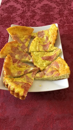A white rectangular plate with several slices of a baked dish, possibly a quiche or frittata, on a table with a red patterned tablecloth. - B&B Rialto Dream (Venice)