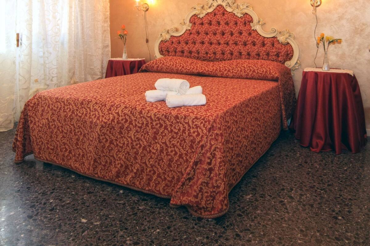 Ein Hotelzimmer mit einem großen Bett, einer Kristallleuchter, zwei Nachttischen mit Lampen und einem roten Vorhang.