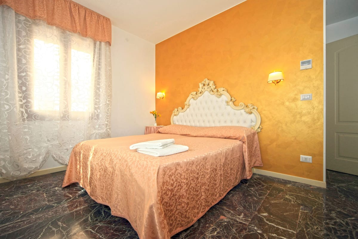 Ein Hotelzimmer mit Bett, Vorhängen, einer Wandleuchte und einem Marmorboden.