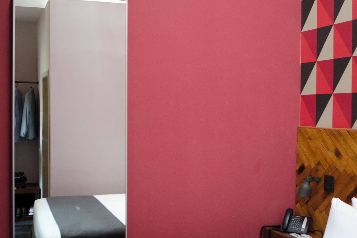 A hotel room with a bed, a large mirror, a wardrobe, and a wall with a geometric pattern.