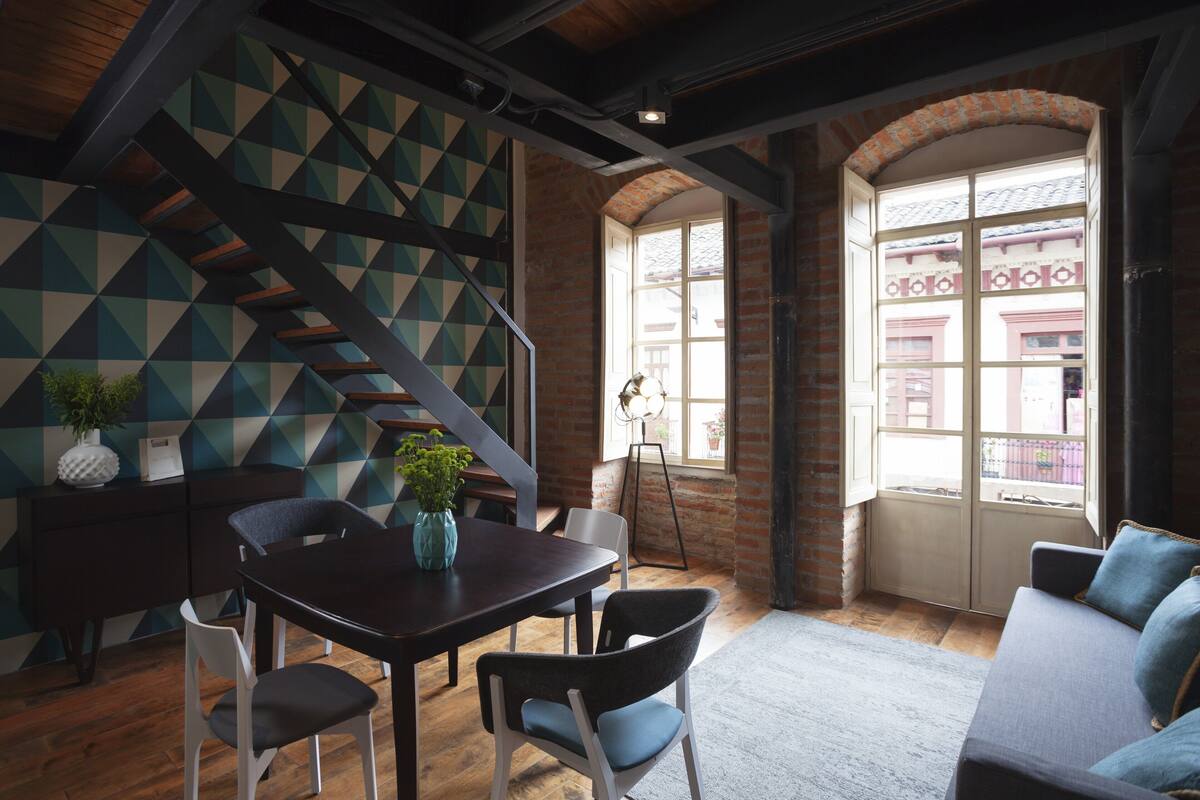 A dining area with a dark wooden table, white chairs, and a geometric-patterned wall.