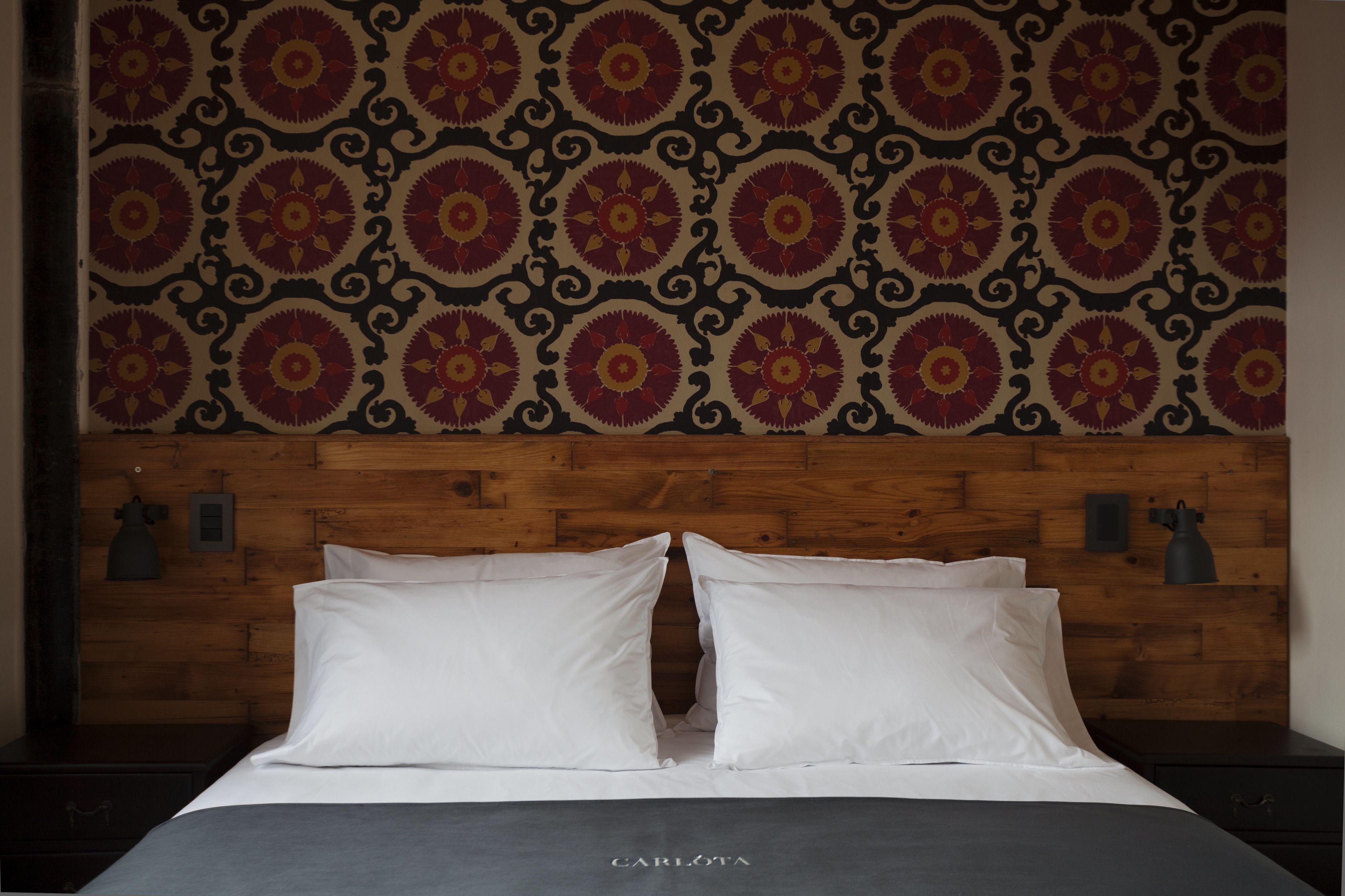 Een hotelkamer met een houten hoofdeinde, behang met een patroon en een bed met witte lakens.