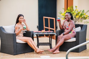 Two individuals seated on wicker furniture outdoors, with a table between them. - Valley Breeze Guest House (St. Andrew)