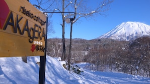 A wooden sign with "Nisekoi" and "AKAGERA" written on it, with a snowy landscape and a mountain in the background. - Niseko Cottage Akagera (Kutchan)