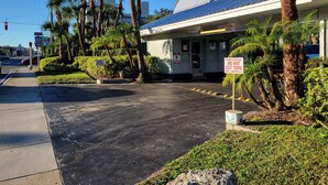 A building with a metal roof, palm trees, and a sidewalk. - Budget Inn Winter Haven (Winter Haven)
