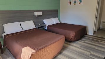 A hotel room with two beds, a nightstand, and a wall-mounted light. There are three framed pictures on the wall.