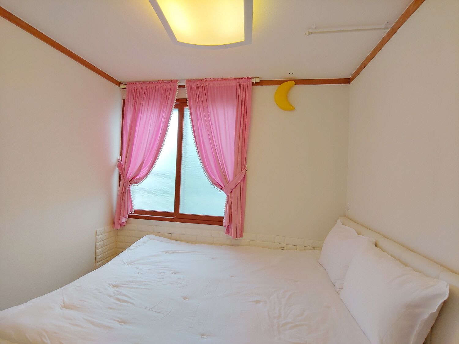 Una camera da letto con un letto, tende rosa, una decorazione a forma di crescente lunare e un lucernario.