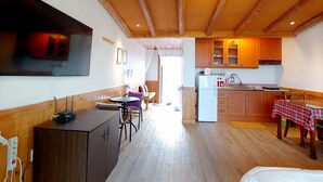 Ett mysigt rum med ett träpanelat tak, ett matbord med en rutig duk, en köksdel med träskåp och en tv som är monterad på väggen.