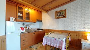 A compact kitchen with wooden cabinets, a white refrigerator, and a dining table with a pink tablecloth.