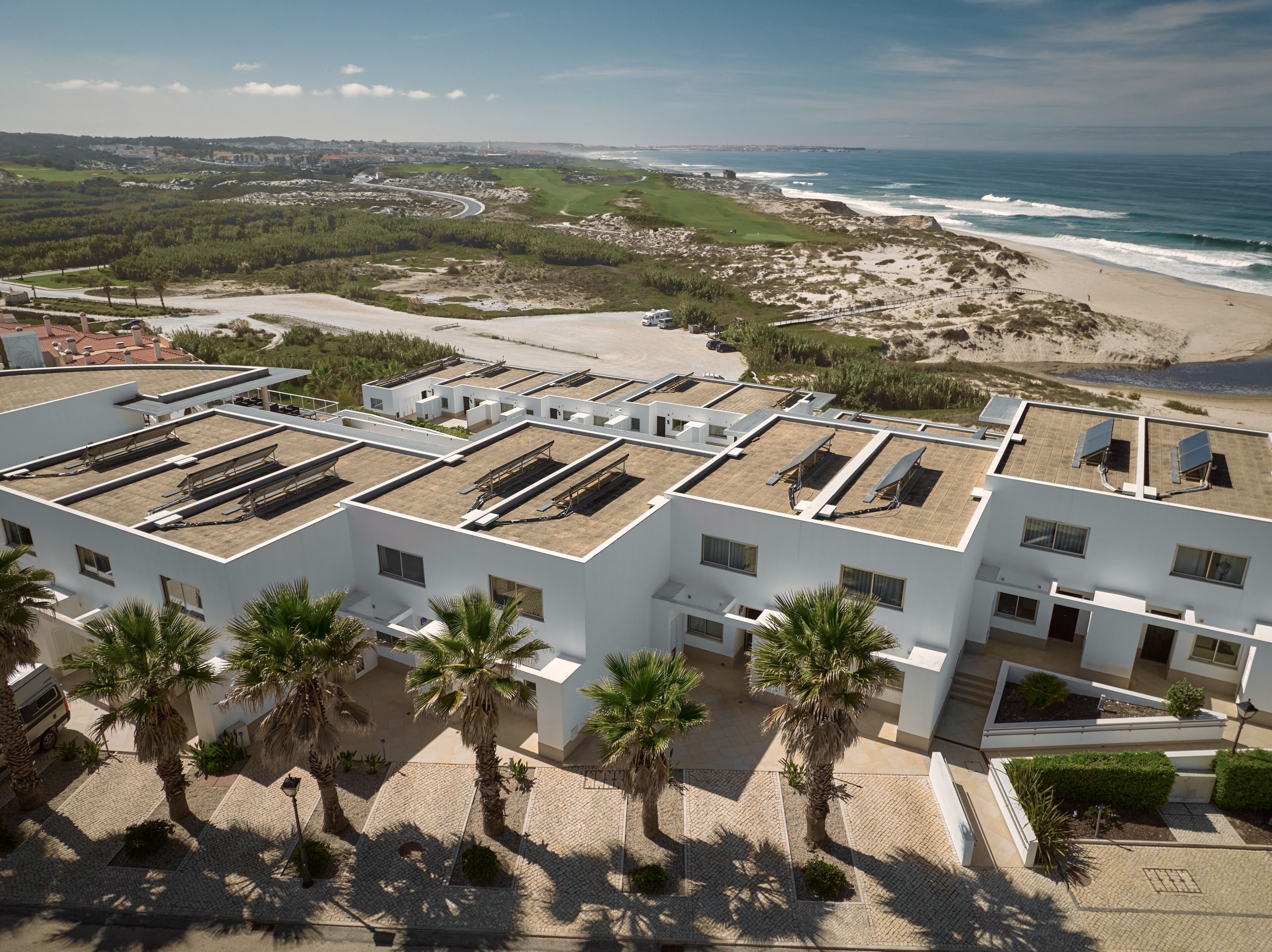 A modern building with a flat roof, solar panels, and a paved courtyard with palm trees.